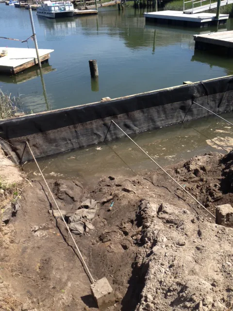 A new bulkhead wall set along a canal with the ground behind it excavated for backfill